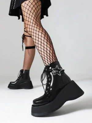 Black glossy patent leather heelless booties back view showing thick platform sole and star ornament with model in fishnet stockings and black skirt