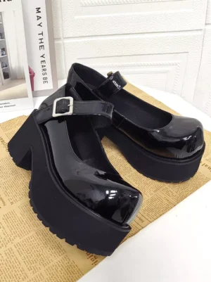 Black glossy patent Mary Jane lolita platform shoes featuring silver buckle ankle strap and chunky platform sole shown in three-quarter side profile on newspaper background