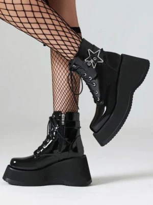 Black patent leather platform heelless booties side view with silver star buckle detail and thick wedge sole on model wearing black fishnet stockings