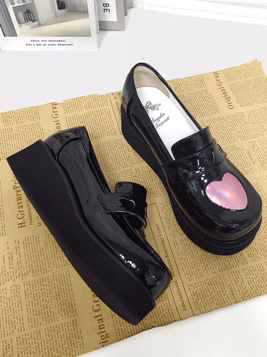 Paired black patent leather Sweet Lolita platform pumps mixed angle view on newspaper background displaying branded insole and holographic heart buckle straps