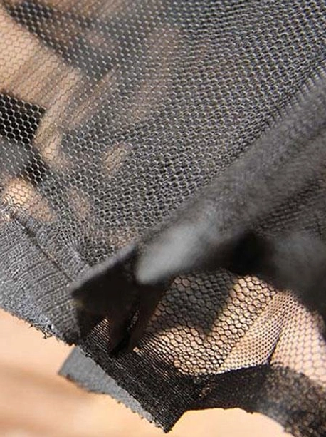 Low angle close-up of black tulle petticoat hem detail showing uneven ruffled skirt edge and sheer mesh fabric construction