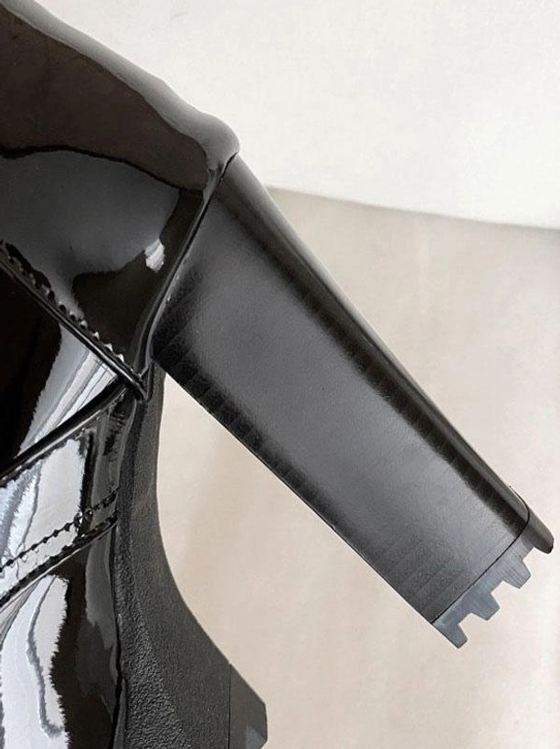 Black mid-calf boot chunky block heel and platform sole close-up low side angle on light gray background, showing platform construction detail