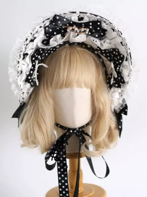 Black polka dot lolita bonnet front view with ruffled eyelet lace, pearl trims, and decorative chin straps on mannequin with blonde wig