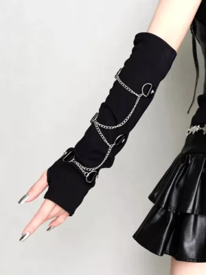 Black punk fingerless arm sleeves featuring asymmetrical silver chain embellishment and rivet details, side profile view of single arm on model wearing leather ruffle skirt, showcasing chain placement