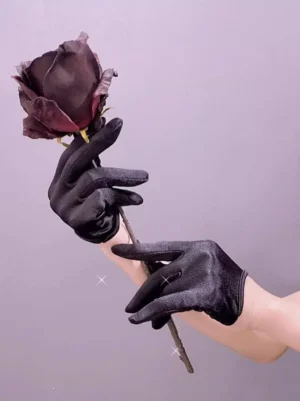 Black satin short gloves close-up side view held with dark rose on purple background showcasing glossy fabric texture and wrist-length design for gothic lolita fashion