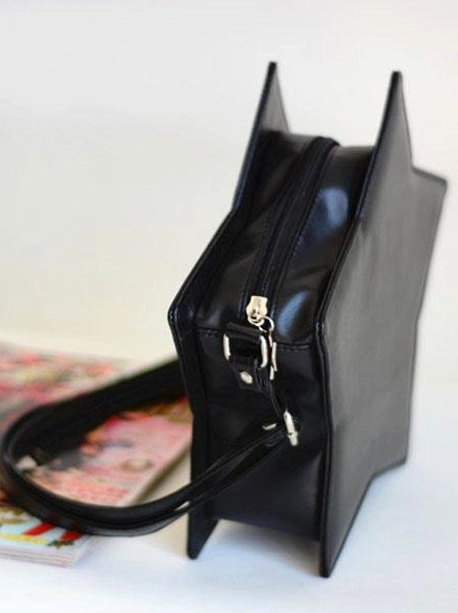 Black star-shaped lolita crossbody bag low three-quarter back view with metal zipper hardware details central zipper pocket displayed with tabletop magazine decor