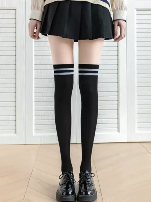 Black striped over-the-knee lolita socks with light gray stripes worn with pleated skirt and patent leather Mary Jane shoes full leg view