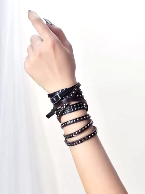 Overhead side view of studded leather wrap bracelet on female forearm, displaying layered wrapping style with silver rivets and buckle fastening, gothic lolita fashion accessory