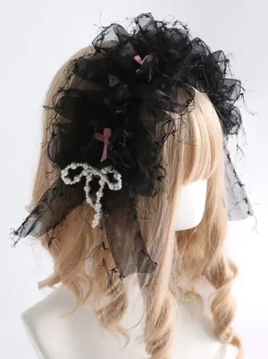 Black sweet lolita ruffled organza headdress with pearl bow accents and pink bow ornaments worn on mannequin with blonde curly wig, three-quarter side view showing delicate frayed tulle edges