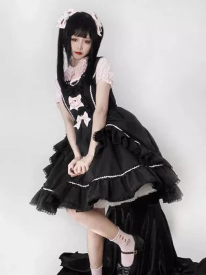 Black Sweet Lolita sleeveless jumper dress with ruffled lace hem and pink bow accents, front full-body view on model