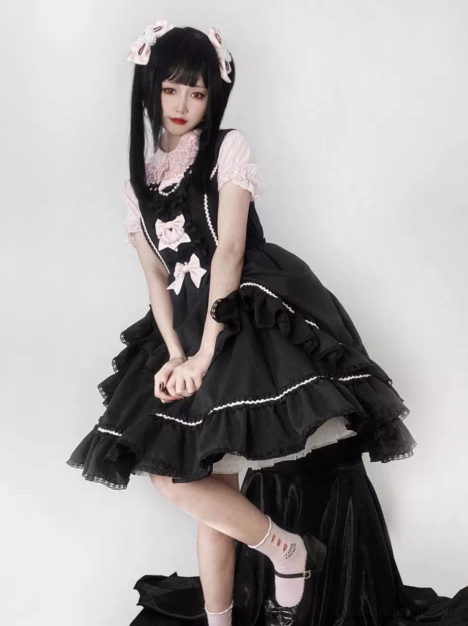 Black Sweet Lolita sleeveless jumper dress with ruffled lace hem and pink bow accents, front full-body view on model