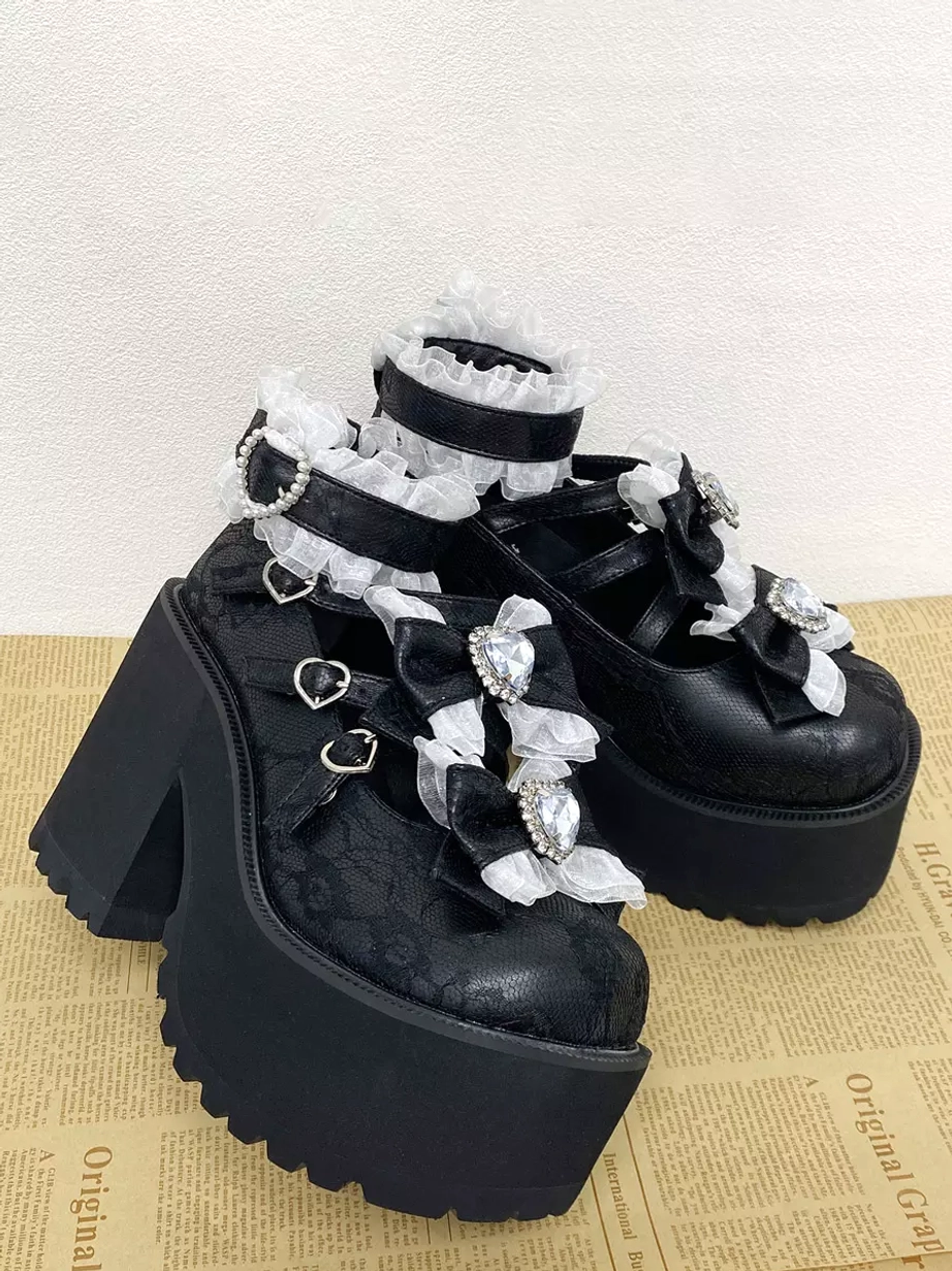 Pair of black sweet lolita platform pumps side three-quarter view vintage newspaper background thick platform heart-shaped buckle straps rhinestone bow details