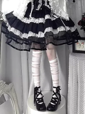 Black and white bandage thigh-high lolita socks worn with gothic platform heels and black dress, front lower-body view showing white wrapped stripe texture