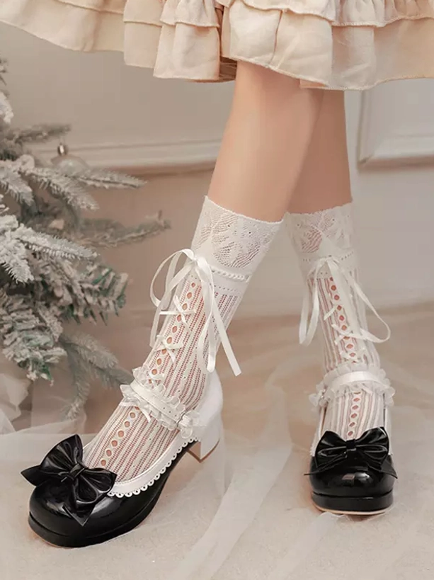 Front full view of black and white Lolita pumps showing prominent black bow decoration at toe, patent leather construction, chunky block heel, worn with beige ruffled skirt