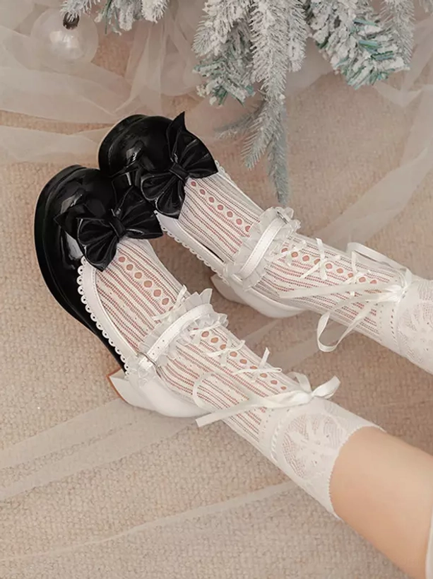 Flat lay top-down view of black and white Lolita Mary Jane pumps paired with white lace ribbon socks, bow decorations, patent leather finish, styled on decorative backdrop