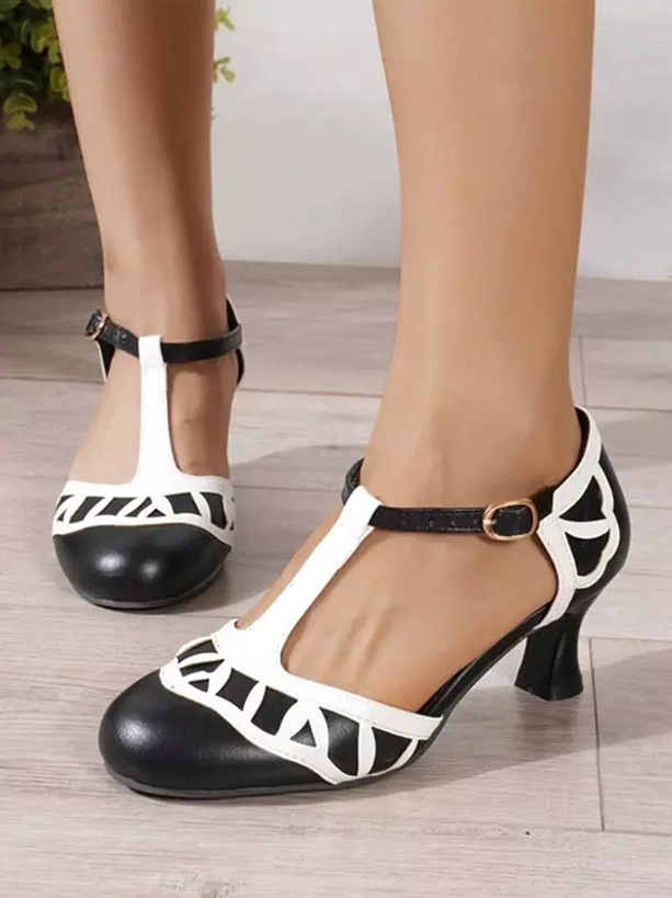 Black and white T-strap Lolita pumps with geometric cutouts and round toe, front close-up view showing decorative patterns and buckle design