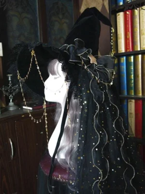 Black star-dotted mesh veil lolita witch hat with gold decorative chain, left profile on mannequin against vintage library backdrop