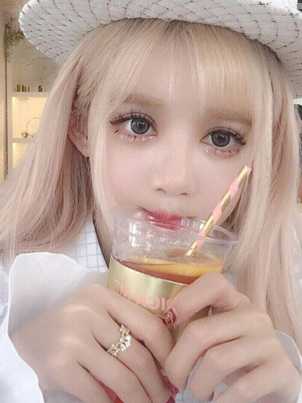 Pale blonde lolita wig with neat air bangs and soft long wavy texture on model in white woven hat holding drink, shop background, sweet lolita wig styling demonstration with ash blonde color