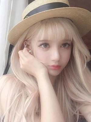 Long blonde lolita wig with air bangs and loose wavy hair styled on female model wearing straw boater hat, indoor curtain background, frontal close-up showing pale blonde color and romantic sweet lolita aesthetic