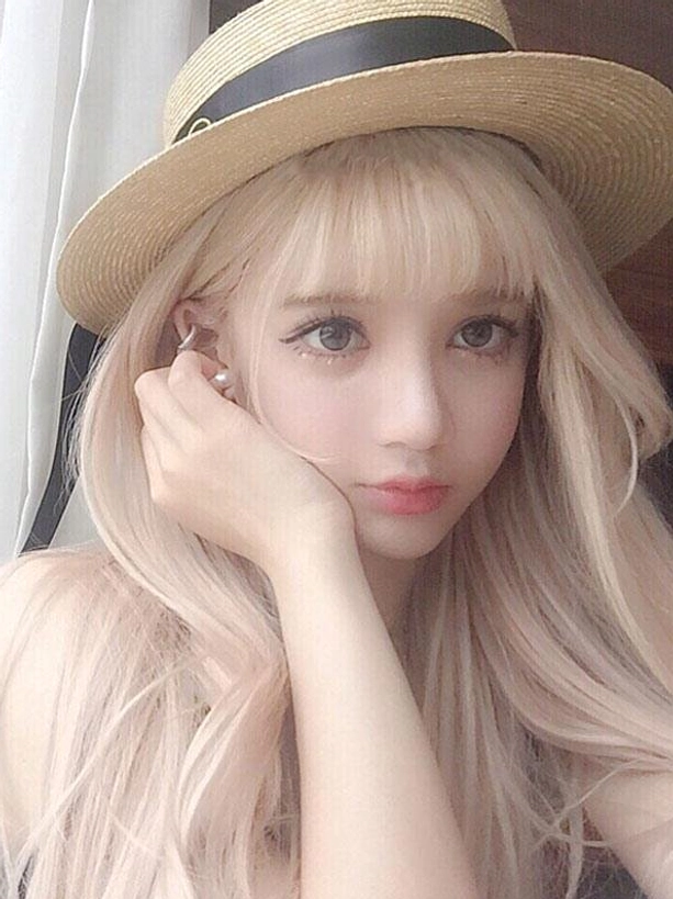Long blonde lolita wig with air bangs and loose wavy hair styled on female model wearing straw boater hat, indoor curtain background, frontal close-up showing pale blonde color and romantic sweet lolita aesthetic