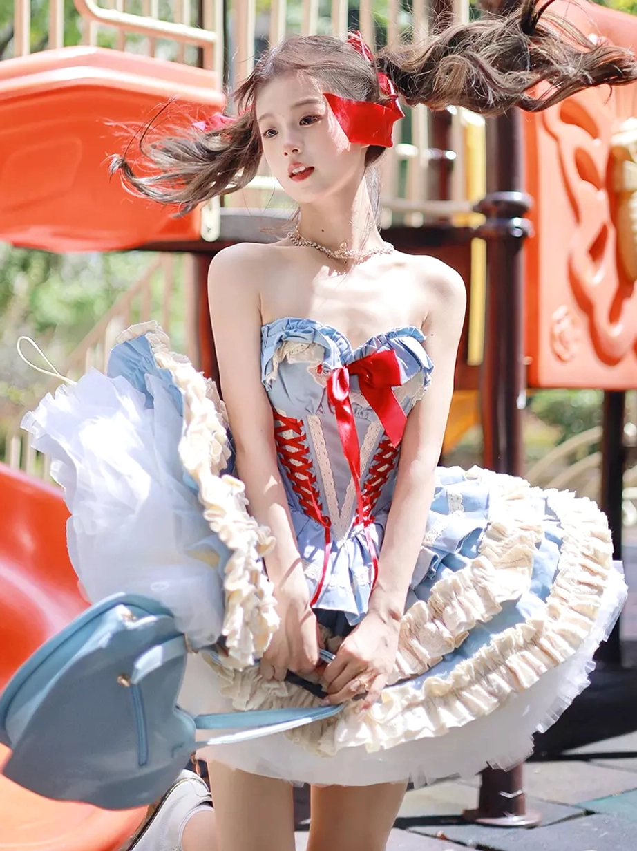 Front seated view of blue ballet lolita dress on outdoor playground, showing blue heart-shaped handbag, red bow lace-up top, and tulle layered skirt details