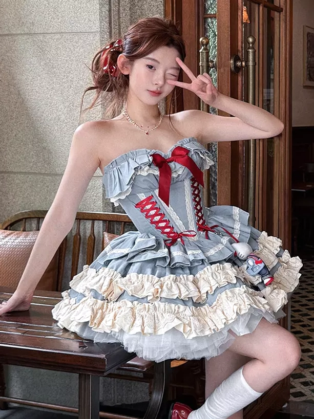 Side three-quarter view of blue ballet lolita dress in vintage indoor cafe setting, featuring red hair ribbon accessory, white knee-high socks, and red bow front details