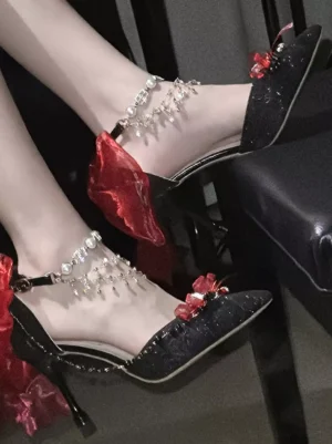Blue glitter pointed toe Lolita stiletto shoe with pearl ankle chain and decorative bow on black furniture, side close-up view