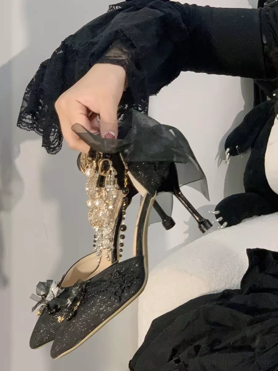 Blue lolita shoe with black lace upper, large decorative bow, pearl chain and stiletto heel held in hand on tabletop