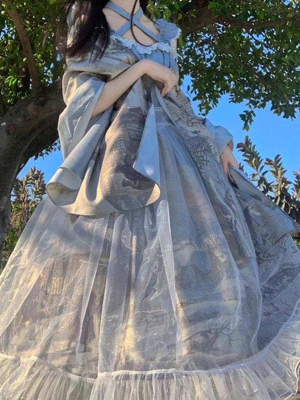 Blue lolita dress with detachable sheer chiffon shawl overlay and landscape print pattern, ruffled hemline, side view outdoor styling under natural tree setting