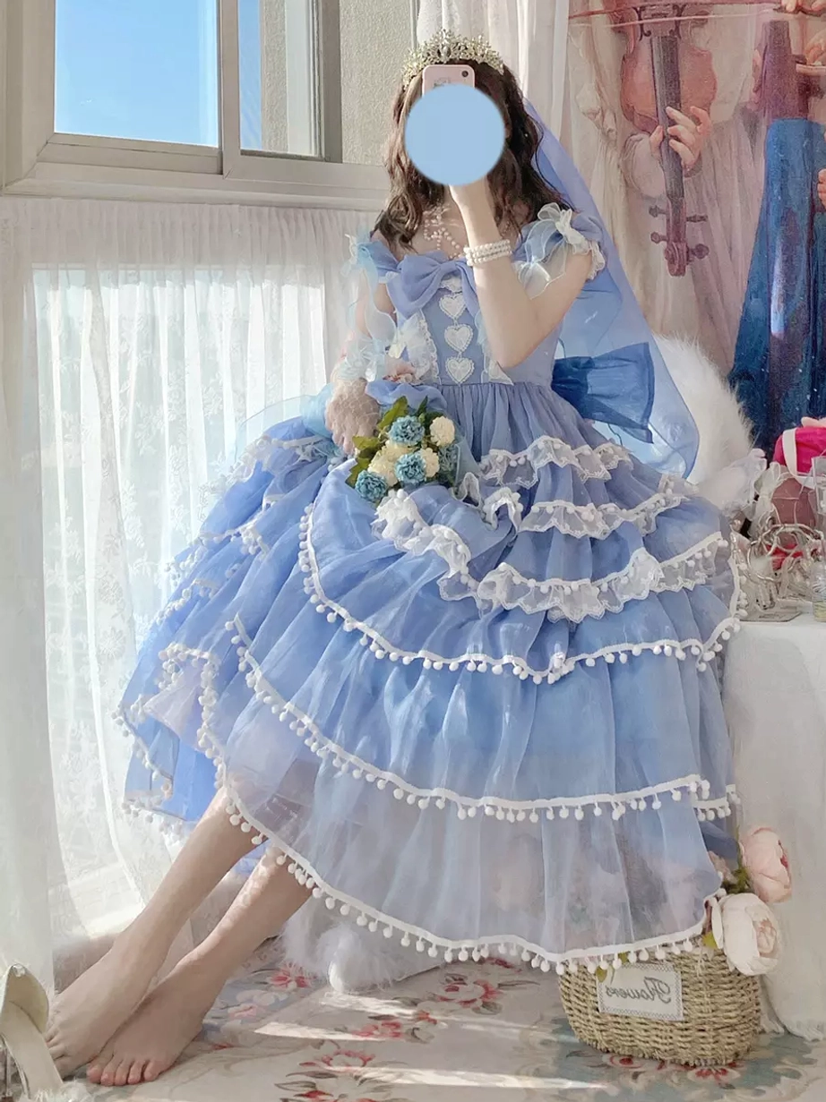 Blue lolita formal wedding dress with tiered tulle construction shown in side sitting pose with tiara, veil, and bouquet