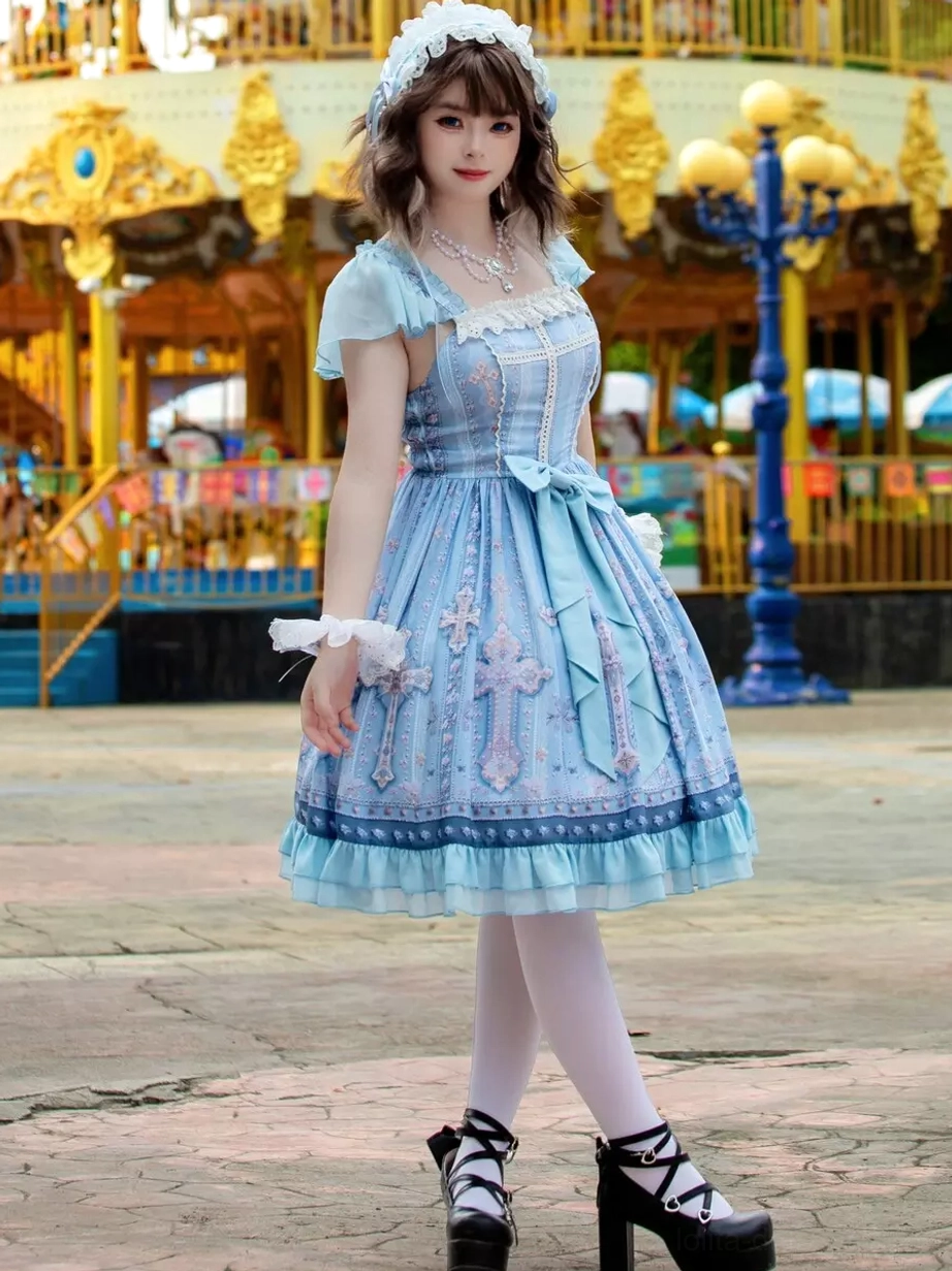 Blue sweet lolita JSK dress full front view with ruffled wrist cuffs, square neckline, bordered skirt trim, cross printed pattern, and front waist bow detail on model carousel backdrop