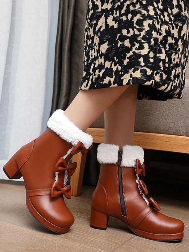 Brown Lolita ankle boots on model feet side view indoors showcasing bow ornaments, fuzzy fur cuff, comfortable block heel, and side zipper