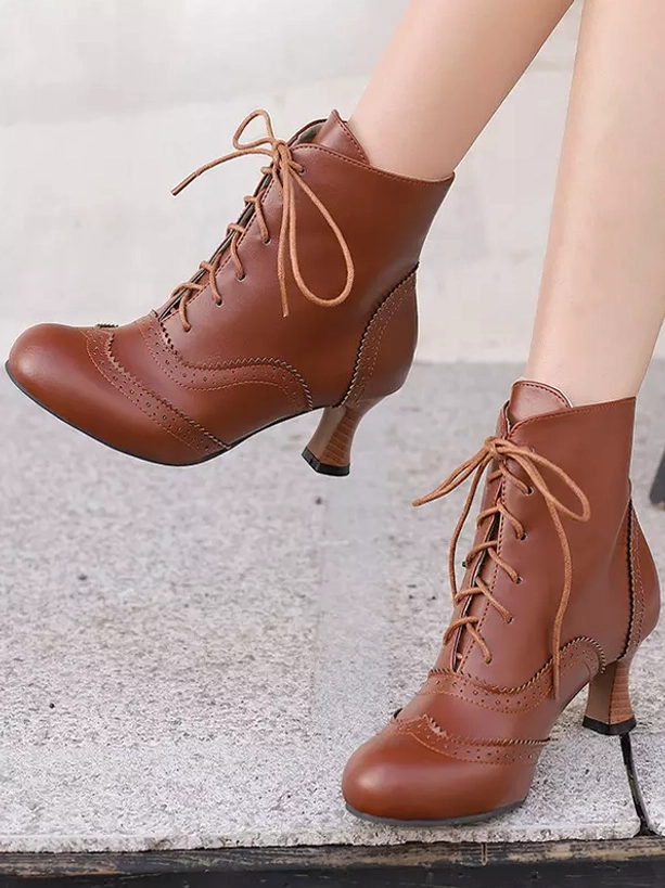Brown Lolita ankle boots displayed from side and lifted boot perspective on female legs, showing round toe shape, brogue perforations, and chunky heel on outdoor concrete platform
