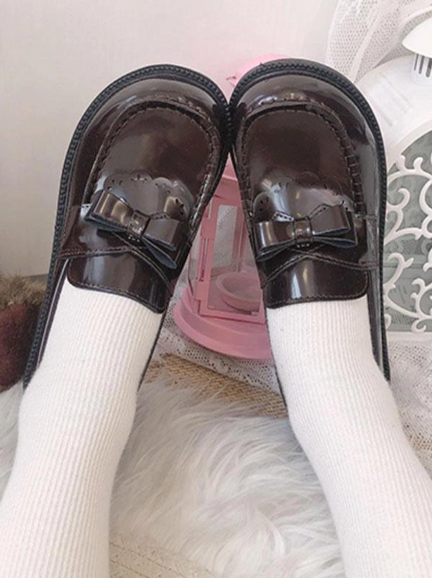 Close-up top view dark brown patent leather bow loafers on furry rug with pink props, glossy round toe lolita footwear