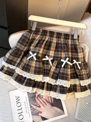 Brown tartan plaid ruffle tiered lolita mini skirt with white lace hem and ribbon bows displayed on wooden hanger showing sweet lolita aesthetic