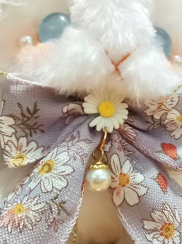 Close-up front view of bunny bag featuring blue glass eyes, daisy bow with pearl pendant, and floral fabric pattern detail on plain background