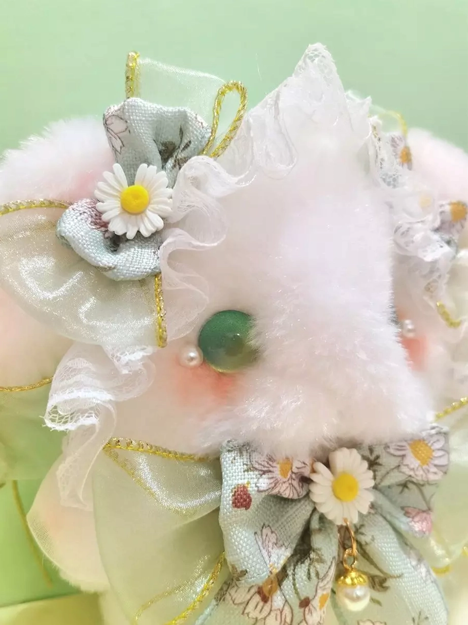 Close-up front view of bunny bag face featuring gold-edged sheer ribbons, daisy and pearl bow, expressive green glass eyes, and detailed embellishment craftsmanship