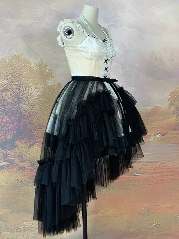 Black asymmetrical tulle skirt with burgundy detachable train and lace-up corset detail displayed on dress form against vintage oil painting background
