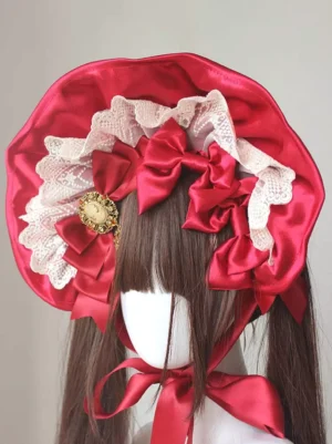 Burgundy gothic lolita ruffled bonnet headdress with satin bows shown on mannequin with twin ponytails and vintage brooch embellishment