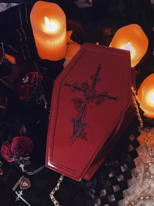Burgundy gothic lolita coffin crossbody bag with black rose cross embroidery, patent PU leather finish, gold chain strap, oblique top view with candles and gothic accessories