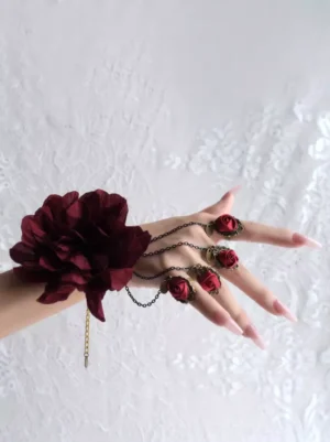 Burgundy gothic lolita hand chain with layered rose flowers and antique bronze chains worn on female hand with nude nails, side front angle on white lace background