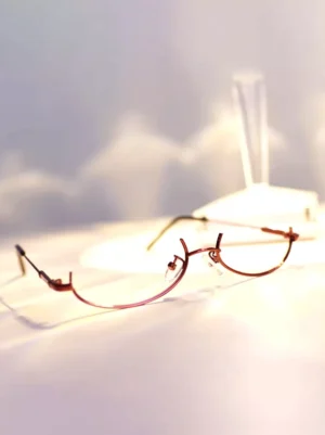 burgundy half-rim cat-eye steampunk lolita glasses with black temple arms displayed on white fabric showing oblique overhead perspective of decorative frame design
