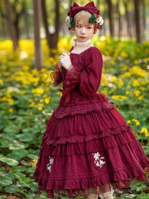 Burgundy Classic Lolita dress with delicate floral embroidery and layered ruffles worn by model in yellow flower field showing half-body perspective with bow hair accessory