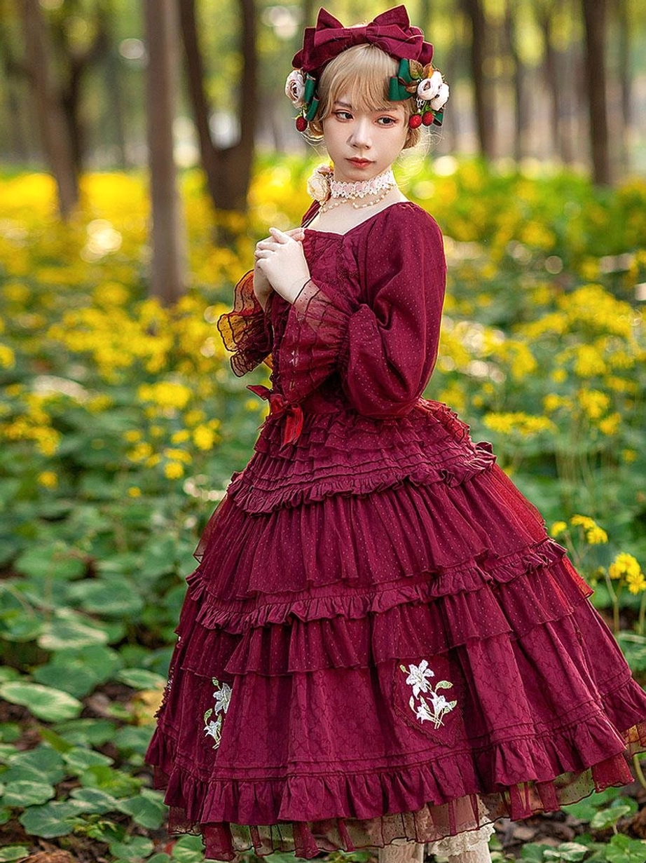 Burgundy Classic Lolita dress with delicate floral embroidery and layered ruffles worn by model in yellow flower field showing half-body perspective with bow hair accessory