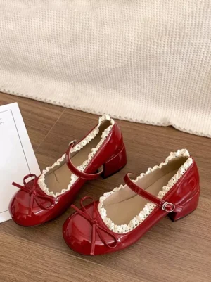 Burgundy patent leather Mary Jane lolita pumps displayed on wooden floor with linen fabric, featuring lace trim, front bow accent, and adjustable ankle buckle strap in flat lay view