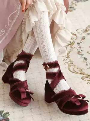 Burgundy lolita block heel shoes with rhinestone bow, lace ankle strap, and peep toe design, worn with frilly lace socks on vintage carpet in overhead side view