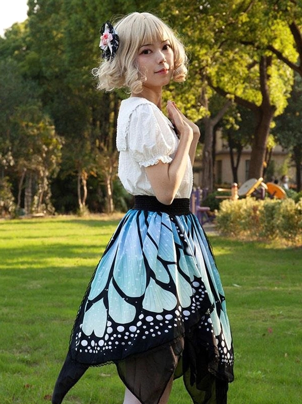 Sweet lolita butterfly skirt outdoor three-quarter view in park setting with model wearing white blouse, showing layered hem and blue butterfly print in natural lighting