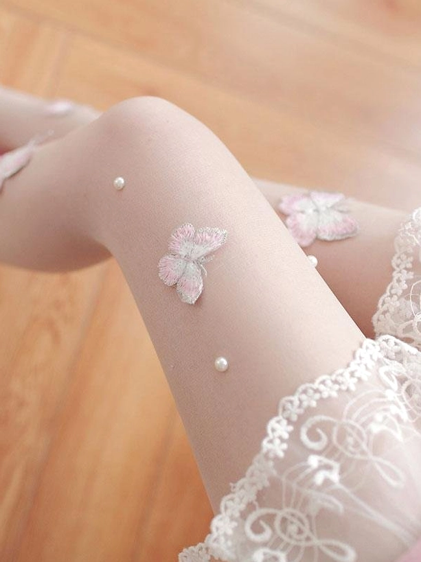 Upper thigh close-up of Sweet Lolita butterfly stockings featuring lace hem, embroidered butterflies and pearl bead accents on wooden floor background