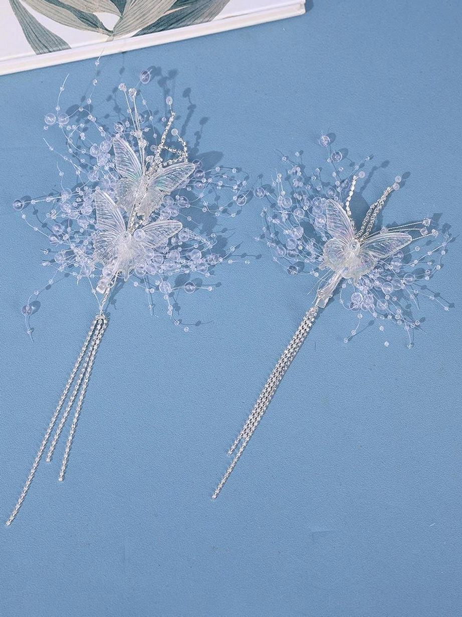 Pair of side hairpins flat lay top view on blue background showing slender crystal branches butterfly design and long tassel pendants