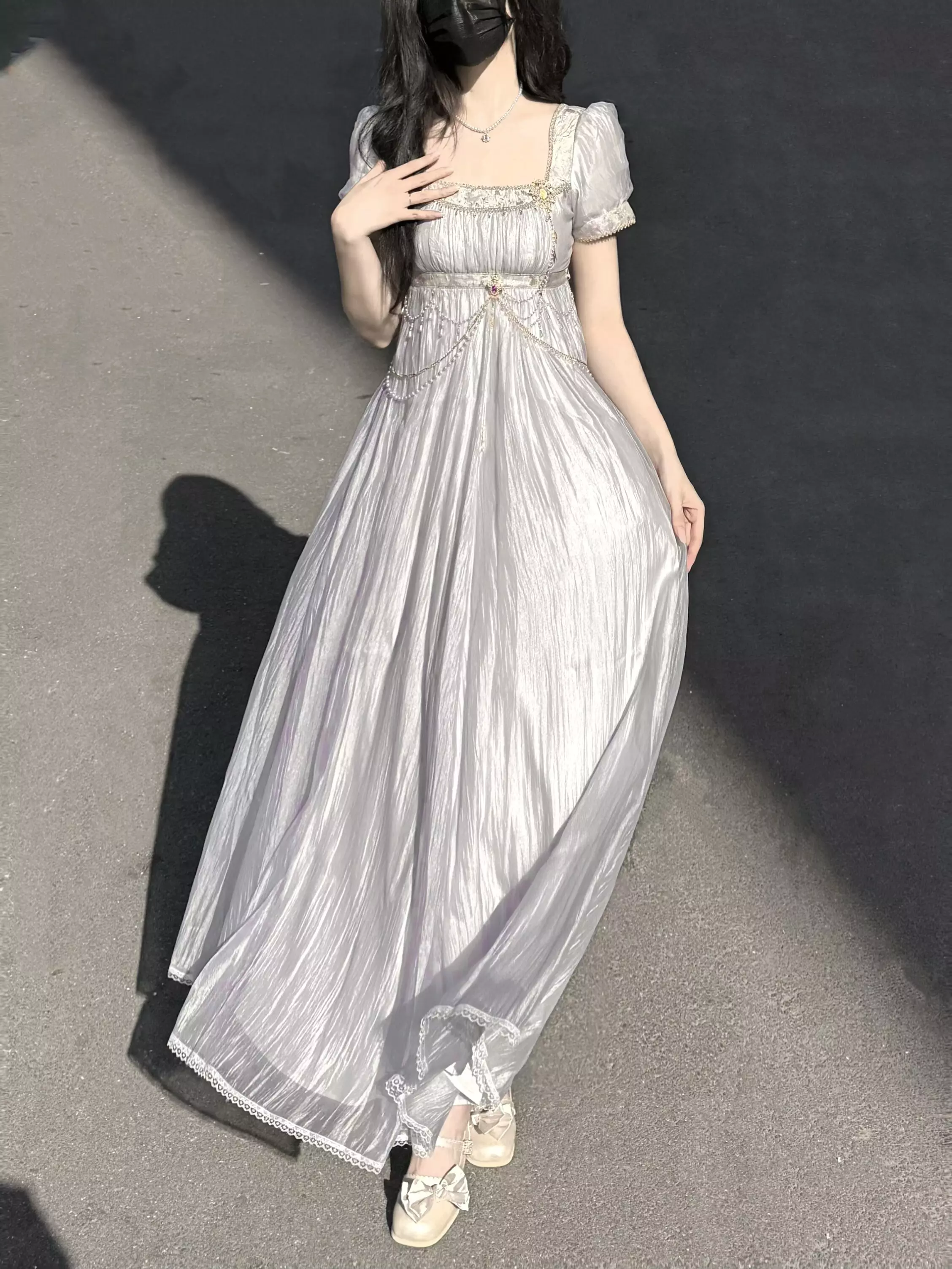 Low-angle side profile of silvery purple Lolita Regency gown with shiny wrinkled fabric, empire waist, floor-length skirt volume, outdoor shaded setting